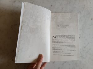 Open page spread of When the Rose Speaks Its Name, held open to the story On Stage Please by SM Lawson, with decorative floral pattern on opposite page and at edges of story page.