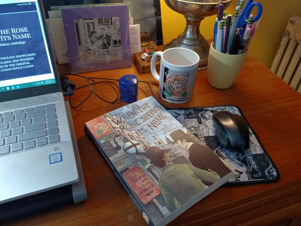 Front cover of When the Rose Speaks Its Name in a cozy library setting with laptop, illustrated mug, mouse, decorative mouse pad, print of an illustration from the book, writing implements and Victorian era vintage lamp. 